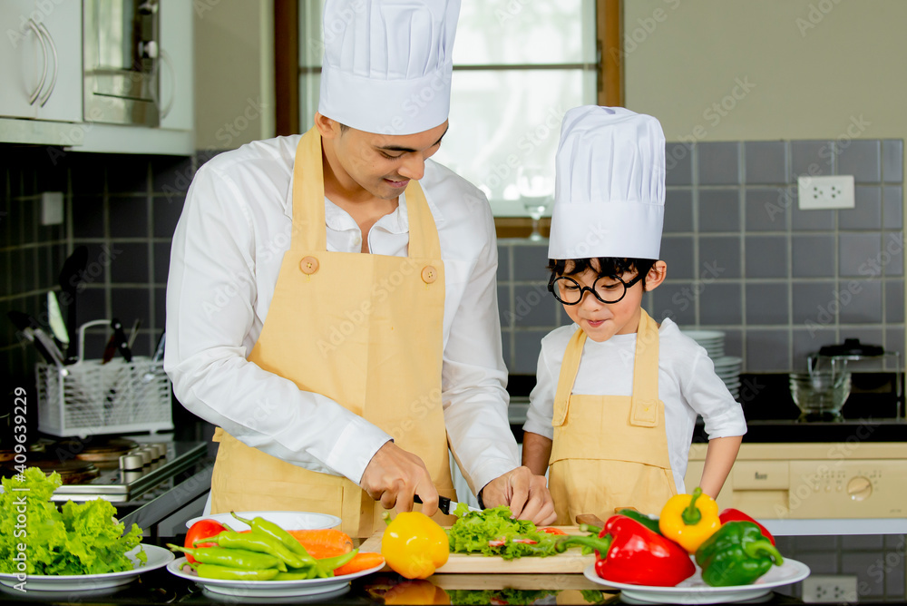 Cute asian little boy with father in uniform chef preparing cooking fresh salad in kitchen at home Cute asian little boy with father in uniform chef preparing cooking fresh salad in kitchen at home