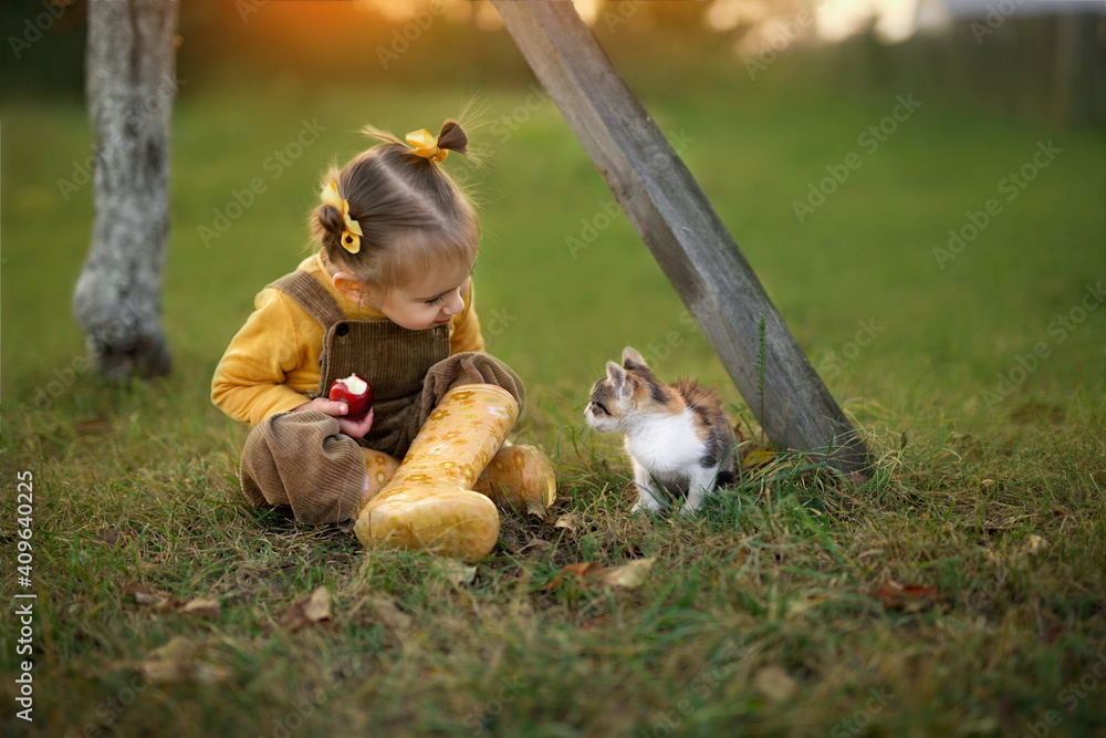 Obraz premium little girl eating red apple. girl sitting with a kitten. the girl wants to feed the cat with an apple. Friendship with pets. World Pets Day. International Homeless Animals Day