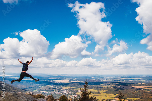 Young man jumps off a cliff into his future. A young boy s giant leap on the Jizera rocks. Up into the clouds. A beautiful panorama of a landscape with clouds and a teenager jumping