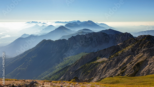 Panoramic view on the haze shrouded valley from the way to Mittagskogel in Austrian Alps. Clear and sunny day. Endless mountain chains. Outdoor activity. Barren top of the mountains  lush lower parts