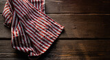 a towel in red and white stripes, lying on a table made of wood with a texture, daylight falls from the window. copy space