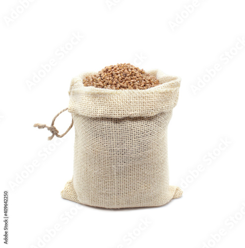 Buckwheat in burlap bag isolated on white background. Raw buckwheat groats in open bag. Close-up. © yulliash