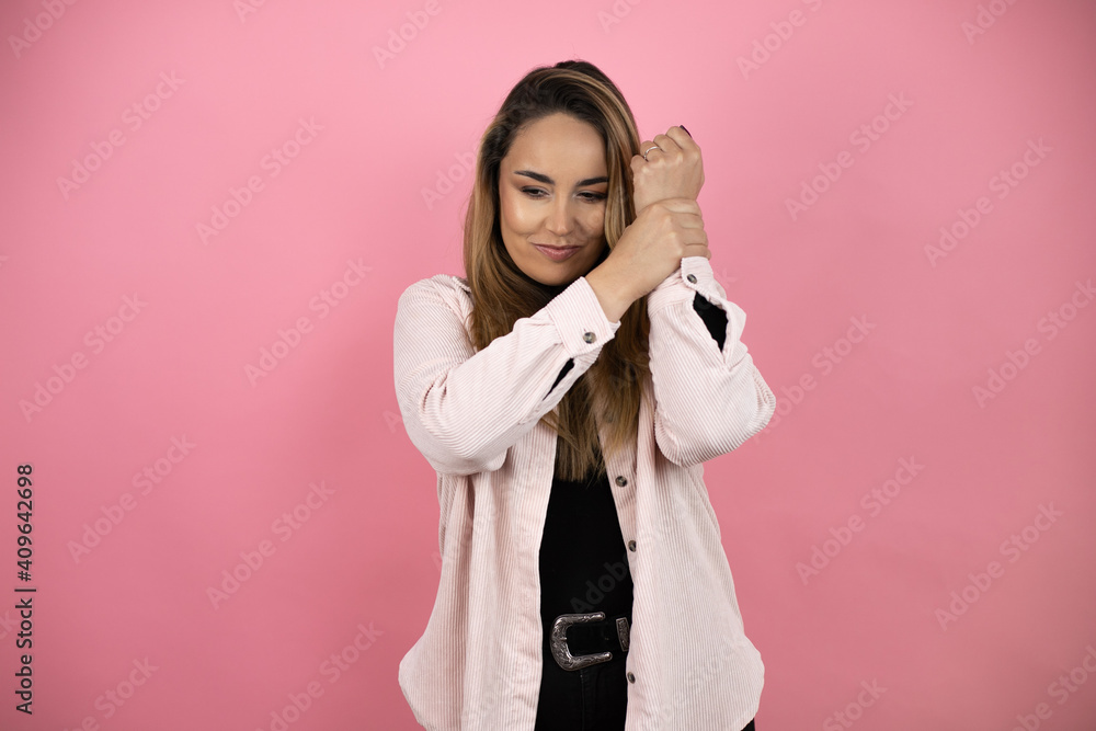 Young beautiful blonde woman with long hair standing over pink background suffering pain on hands and fingers, arthritis inflammation