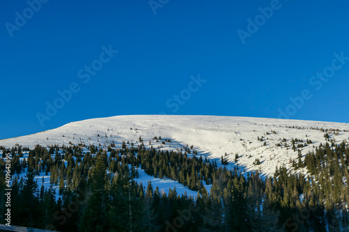 An early, wintery morning in the region of Stubalpe, Austria. The distant mountain peaks are covered with powder snow. There is a dense forest on the lower parts of the slope. Sunny and clear day. photo