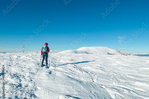 A woman wearing pink jacket and snow shoes hiking up to Amerinkogel s peak in Austrian Alps. Fresh powder snow. Many mountain chains in the back. Winter outdoor activity. Solitude and peace