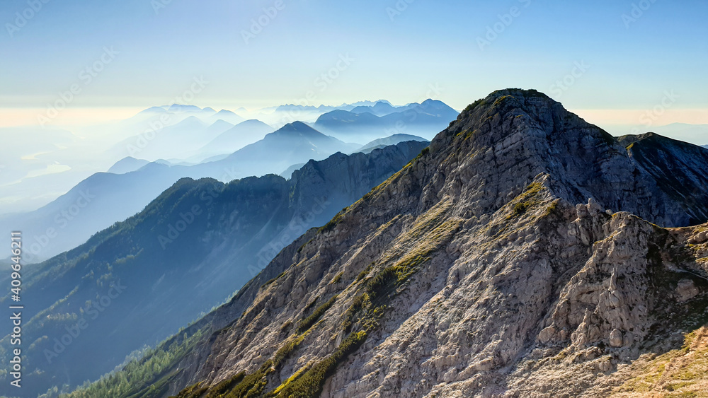 Panoramic view on the haze shrouded valley from the way to Mittagskogel in Austrian Alps. Clear and sunny day. Endless mountain chains. Outdoor activity. Barren top of the mountains, lush lower parts