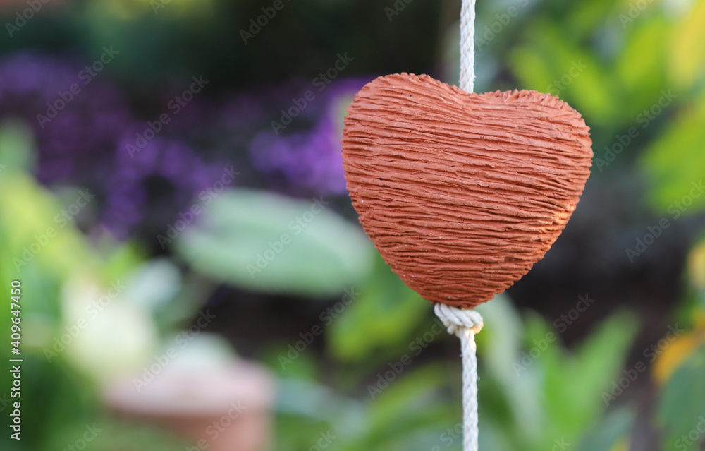 Closeup of brown heart-shape handmade earthenware hanging by white rope with natural background. Closeup of brown heart-shape handmade earthenware hanging by white rope with natural background.