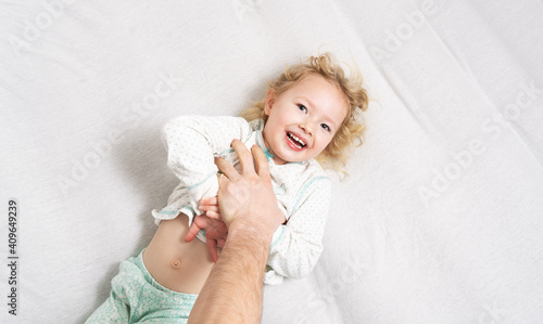 Canvas Print Family time: a little girl lies on the bed and laughs cheerfully because of the tickling of her father