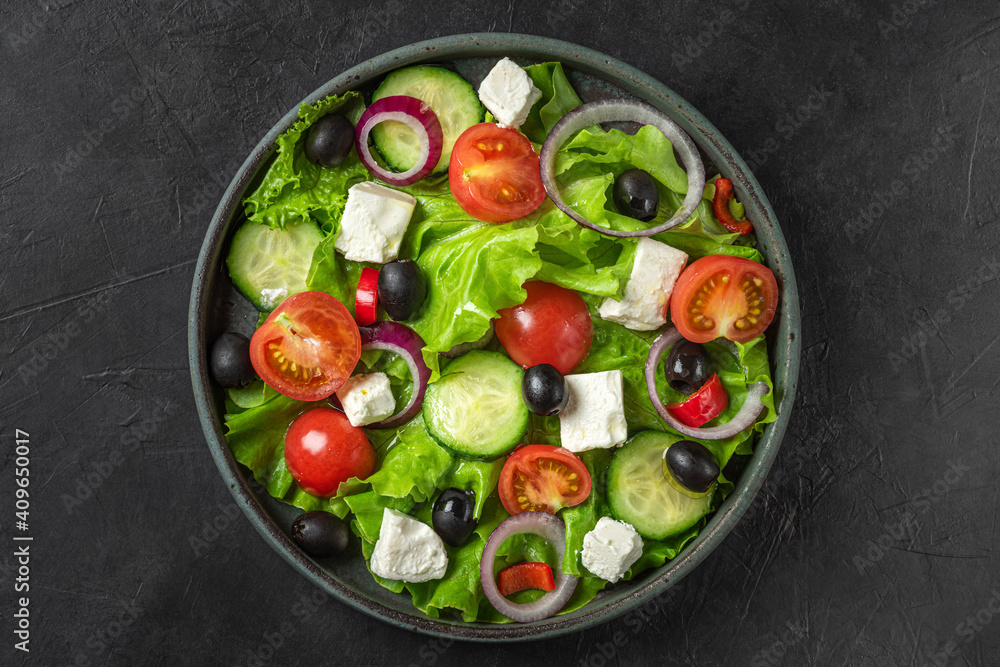 Greek salad with fresh vegetables, feta cheese and olives in a plate on black background. Top view. Vegetarian food