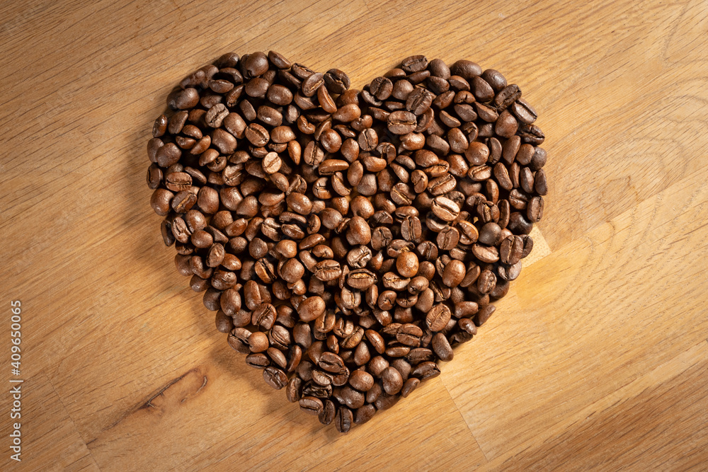 Brown freshly roasted coffee beans shaped into a love heart on oak wood background Brown freshly roasted coffee beans shaped into a love heart on oak wood background