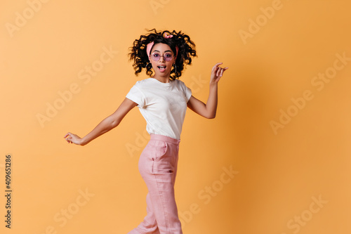 Lovable girl with ribbon jumping on yellow background. Front view of active stylish woman with curly hair.