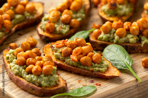 Sweet potato toast loaded with avocado guacamole and baked chickpeas sprinkled with chili flakes served on wooden board