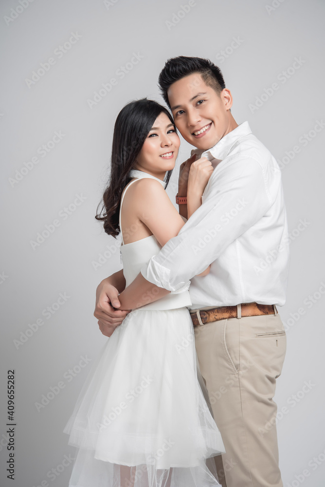 Happy Asian couple in love on gray background. man embracing woman wearing white dress. Happy Asian couple in love on gray background. man embracing woman wearing white dress.