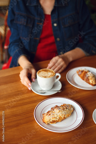person eating breakfast in cafe with coffee in white cup and croissants on white plate. woman with coffee. hands with coffee