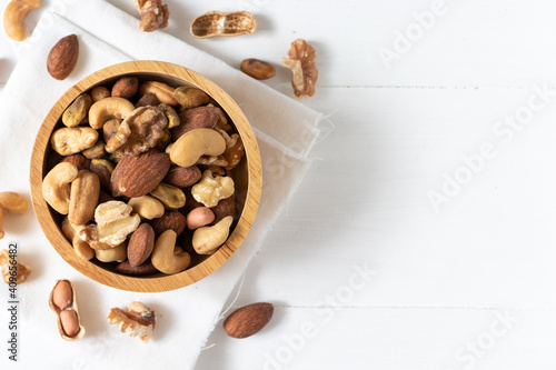 Top view of mixed nuts in a wooden bowl on white background