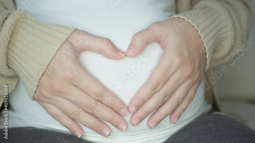 pregnancy, love, people and expectation concept - happy pregnant woman making heart gesture over holidays lights background.