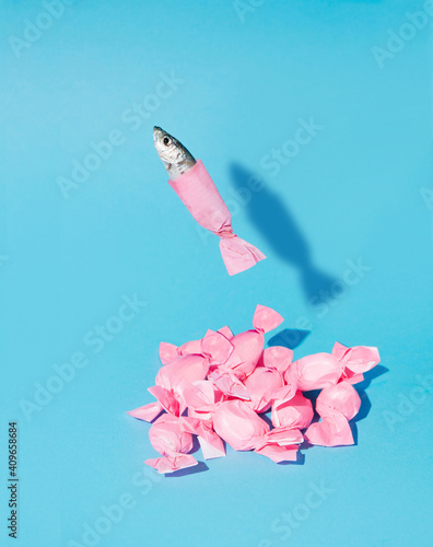 A creative idea of a fish jumping out of the isolation of a pink candy on a cyan background. Minimal aesthetic composition photo