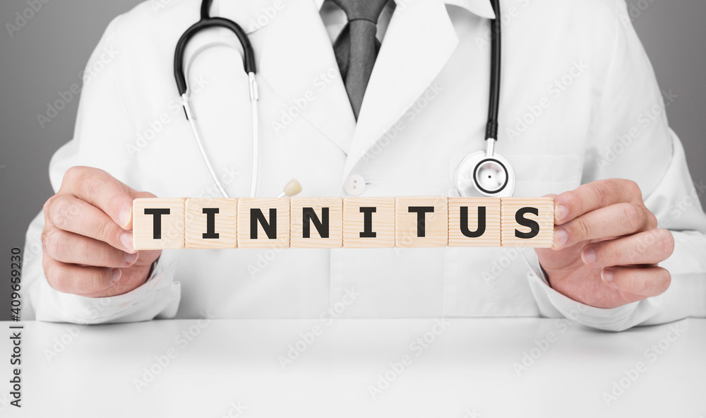 Doctor holds wooden cubes in his hands with text TINNITUS Doctor holds wooden cubes in his hands with text TINNITUS