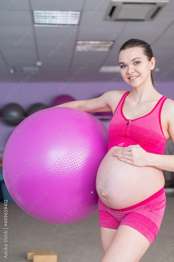 A pregnant woman in sportswear is doing gymnastics for pregnant women. The girl is engaged in fitness with a ball for expectant mothers. Last trimester. A pregnant woman in sportswear is doing gymnastics for pregnant women. The girl is engaged in fitness with a ball for expectant mothers. Last trimester.