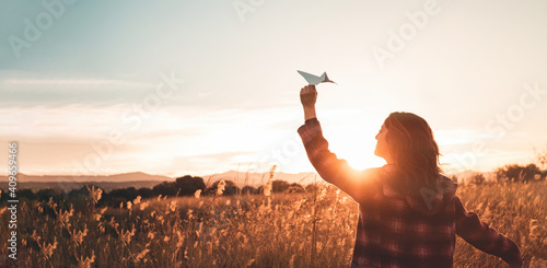 Travelling woman with paper airplane enjoying life and freedom at the land at sunset. Arms outstretched and happiness