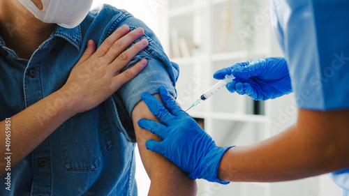 Young Asia lady nurse giving Covid-19 or flu antivirus vaccine shot to senior male patient wear face mask protection from virus disease at health clinic or hospital office. Vaccination concept.