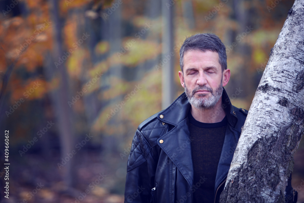 handsome man in leather jacket with eyes closed in the forest handsome man in leather jacket with eyes closed in the forest