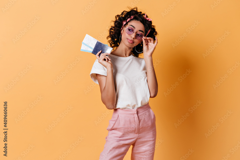 Refined girl holding flight tickets. Studio shot of dreamy young woman with passport standing on yellow background. Refined girl holding flight tickets. Studio shot of dreamy young woman with passport standing on yellow background.