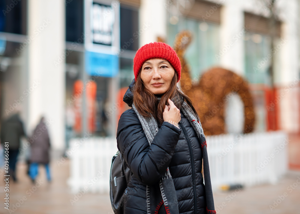 Asian woman in black coat and red hat walking around winter city