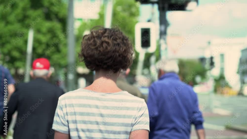 curly haired woman crossing main road at pedestrian crossing in back view curly haired woman crossing main road at pedestrian crossing in back view