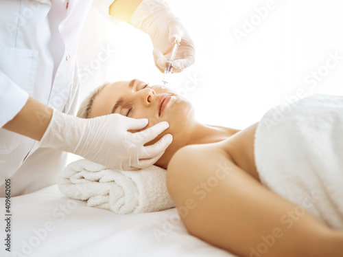 Beautician doctor hands doing beauty procedure to female face with syringe in sunny clinic. Cosmetic medicine and surgery, beauty injections concept