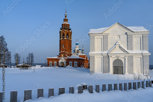 Ancient architecture of Cherdyn (Northern Ural Russia) - cities on 3 hills in winter. Historic center with beautiful churches and houses, a fence, blue skies and deep snow on a winter day.  #409662208