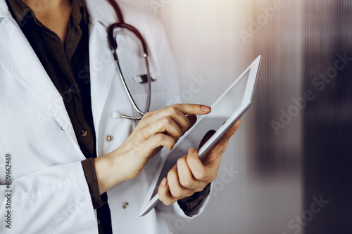 Unknown female doctor using tablet computer in sunny clinic. Medicine concept