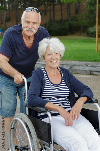 portrait of man pushing disabled wife in wheelchair outdoors