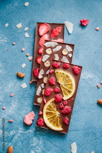 Diet dark chocolate without sugar based on cocoa and stevia with the addition of freeze-dried berries, nuts and fruits. Top view on blue background photo