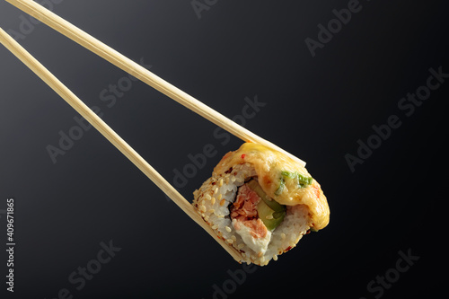 Fresh tasty sushi with wooden chopsticks on a dark background.