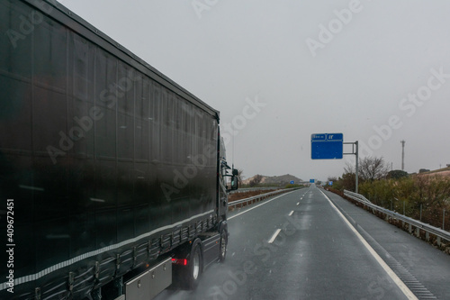 Black truck driving on the highway with the snow falling.