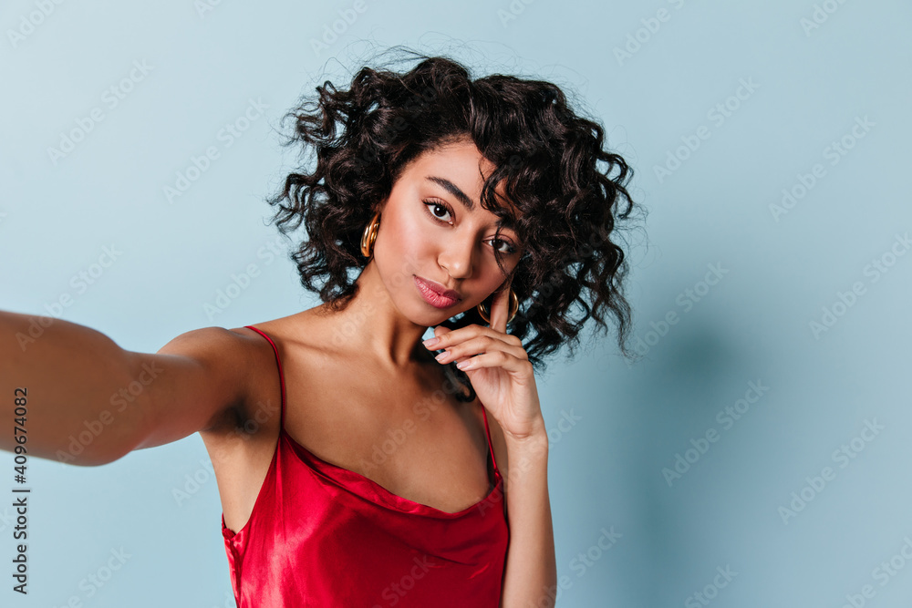 Pensive mixed race girl taking selfie. Studio shot of pretty curly young woman.