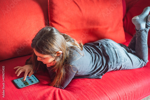Young girl 10 years old is using smartphone on the sofa. Lifestyle, indoors. 
