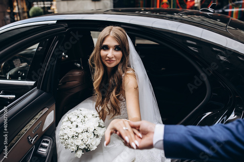 The bride in a white dress is holding a beautiful wedding bouquet. Portrait of the bride. The bride gets out of the black limousine.