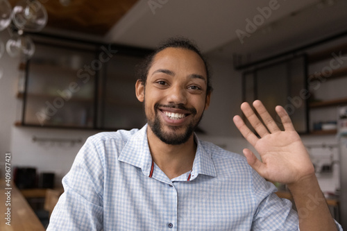 Portrait of positive young black guy look at digital web camera make video call wave hand welcome dialogue partner. Smiling mixed race man blogger start recording content review say hello to audience