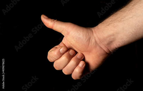 Closeup of male hand showing thumbs up sign against black background