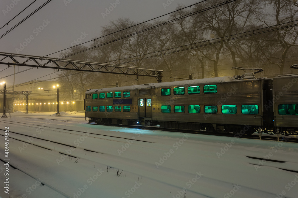 Large passenger train car with green windows at rest in the snow on overcast night in urban Chicago