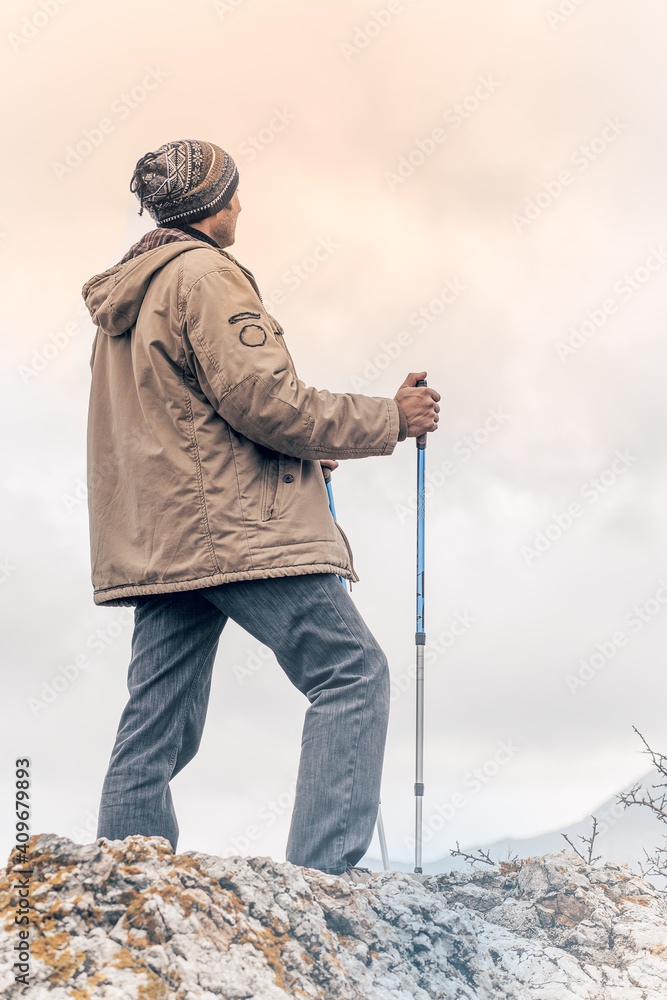 A hiker with sticks in hands enjoys the view while standing at top