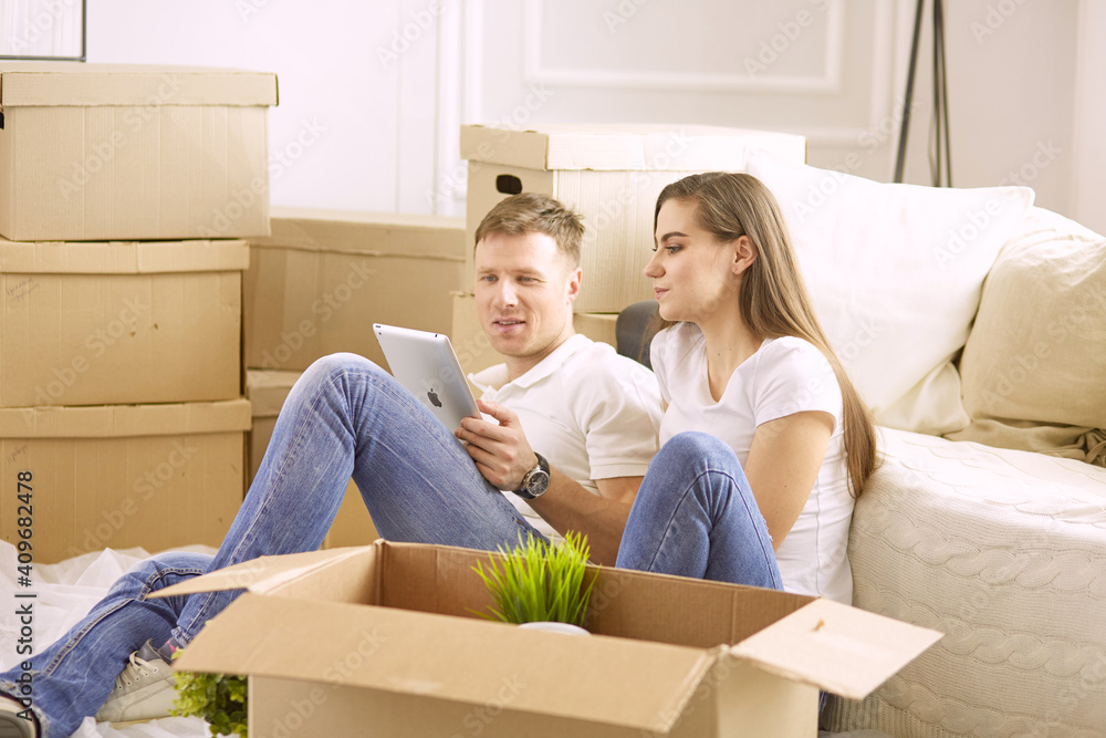 Portrait of happy couple looking at laptop computer together sitting in new house, surrounded with boxes Portrait of happy couple looking at laptop computer together sitting in new house, surrounded with boxes