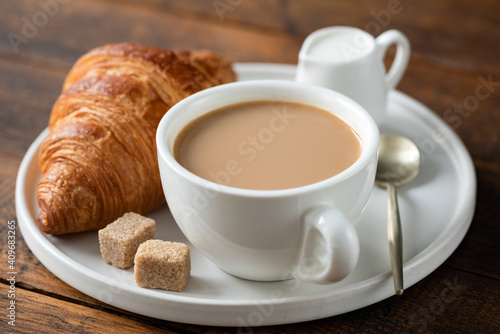 Coffee with milk and french croissant on a plate. Breakfast in cafe on a wooden table background