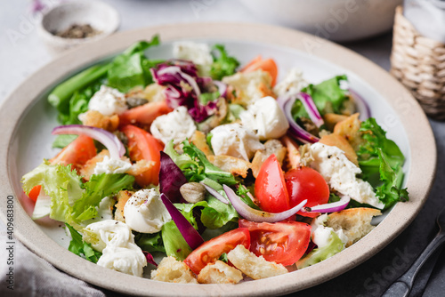 Italian summer salad with mozzarella cheese, green leaf salad, croutons, tomatoes and capers in a bowl. Healthy vegetarian salad