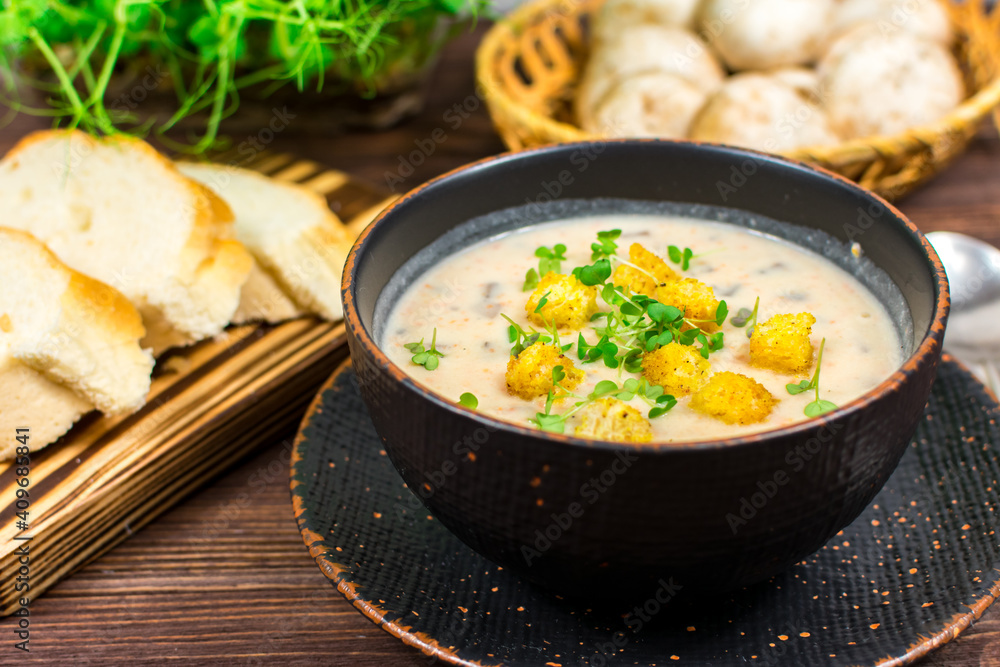 A bowl of homemade mushroom puree soup with herbs and bread on a wooden table. Homemade vegetarian mushroom soup with vegetables and bread. A bowl of homemade mushroom puree soup with herbs and bread on a wooden table. Homemade vegetarian mushroom soup with vegetables and bread.