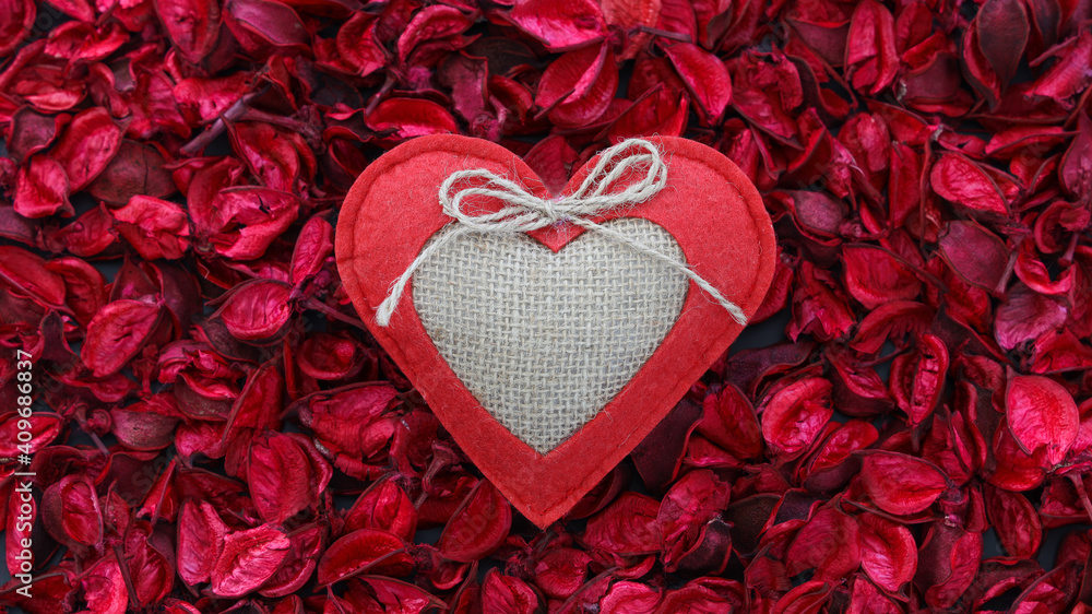 Selective Focus of Handmaded Textile decorative fabric red toy heart among dry pink and red rose petals. Top view of valentine's day background. Selective Focus of Handmaded Textile decorative fabric red toy heart among dry pink and red rose petals. Top view of valentine's day background.