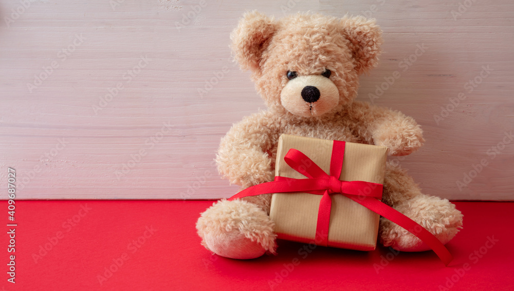 Obraz premium Teddy bear holding a gift box sitting on red floor. Valentines day.