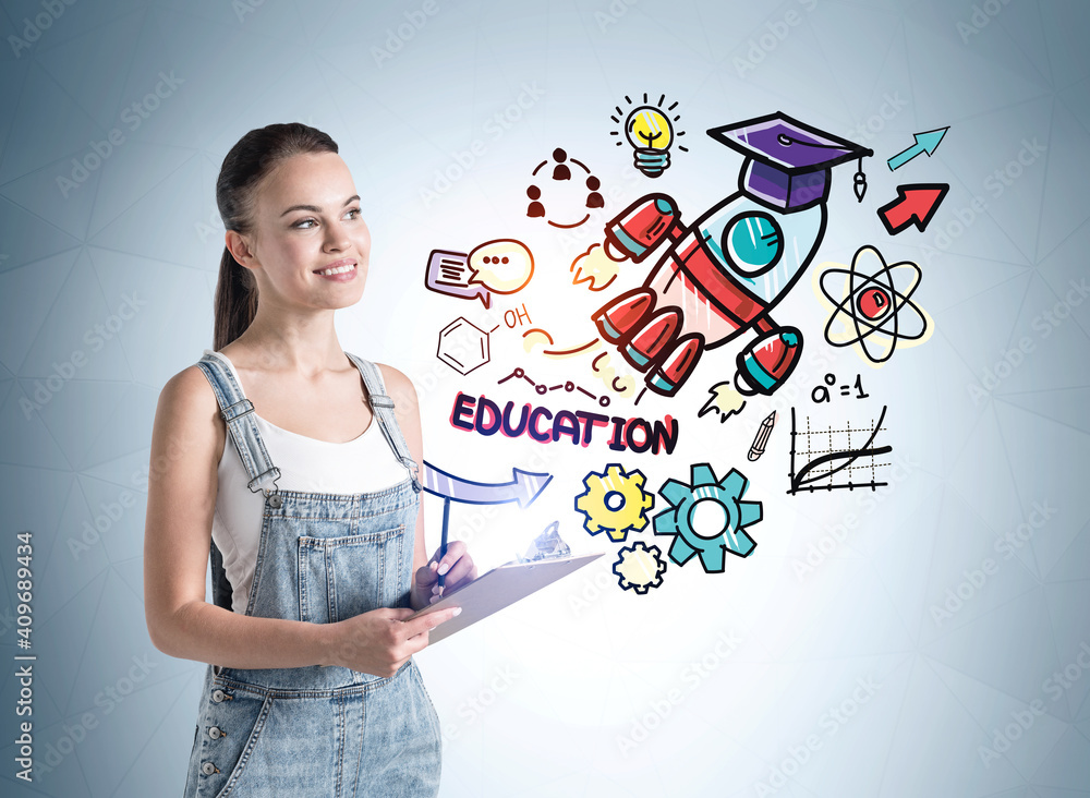 Portrait of inspired young student woman in denim overalls with notebook standing in room with colorful business education sketch drawn on it. Concept of planning and business education Portrait of inspired young student woman in denim overalls with notebook standing in room with colorful business education sketch drawn on it. Concept of planning and business education